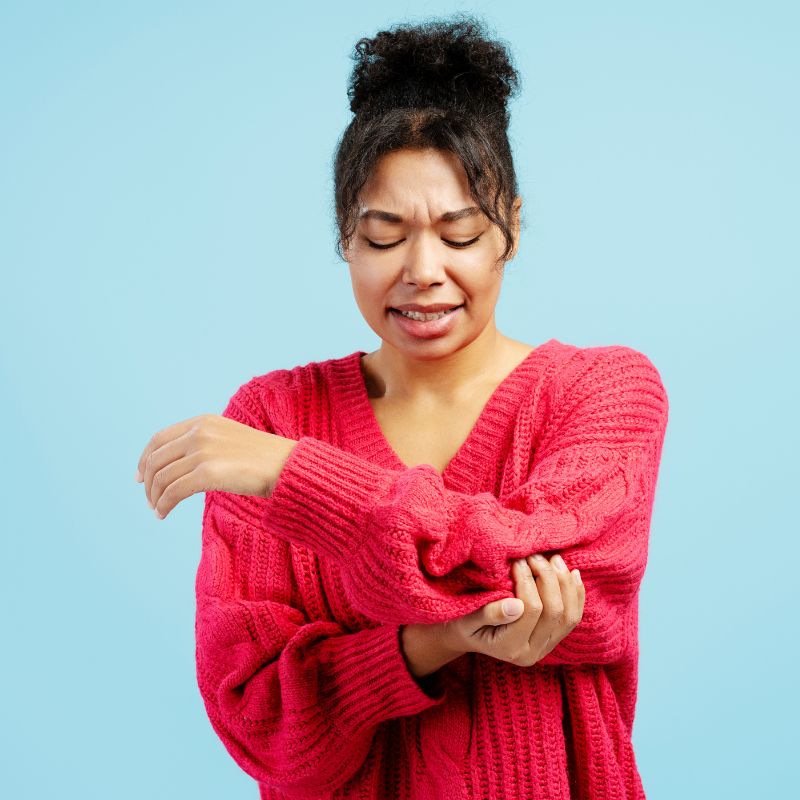 Woman scratching her arm in discomfort, possibly due to a satin allergy or skin irritation from synthetic fabric