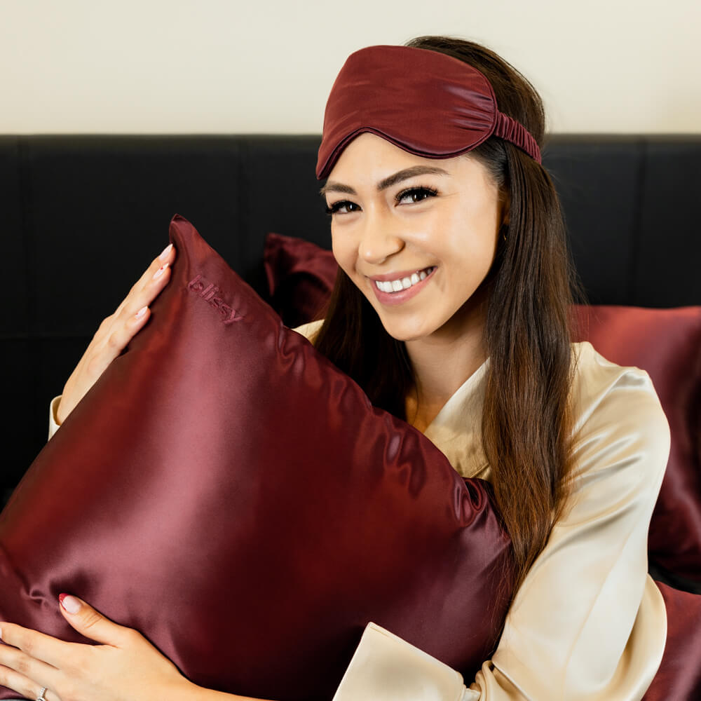 Woman hugging a pillow with burgundy red Blissy mulberry silk pillowcase