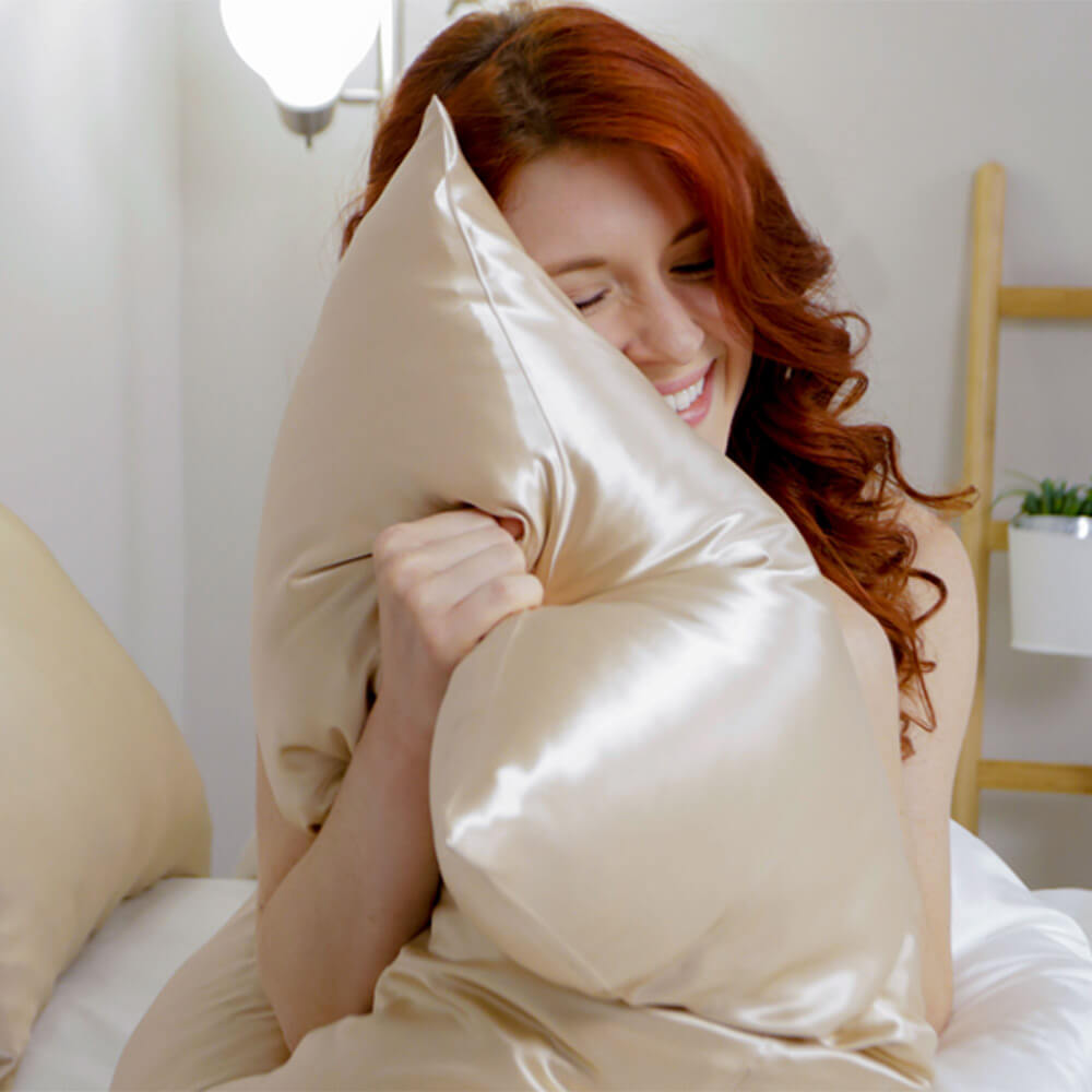 Smiling woman holding a champagne Blissy mulberry silk pillowcase with its box