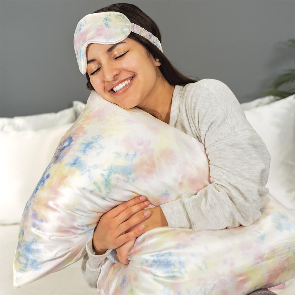 Woman smiling while hugging a pillow featuring tie dye Blissy mulberry silk pillowcase and sleep mask