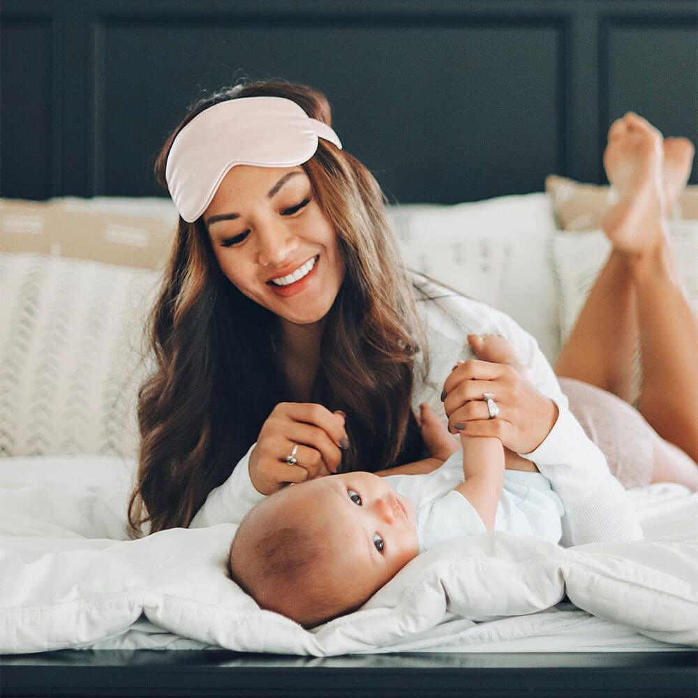 Woman and baby on a bed featuring Blissy mulberry silk pink sleep mask