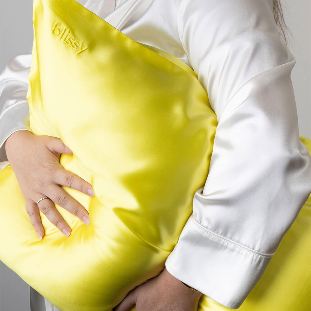 Woman holding a sunshine yellow Blissy mulberry silk pillowcase from Blissy Brights collection