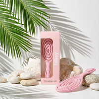 Pink detangling brush with packaging on a light background with stones and leaves